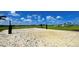 Community sand volleyball court surrounded by green grass, palm trees, and a peaceful lake view at 9292 Tequila Sunrise Dr, Sarasota, FL 34241