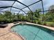 A screened-in pool with a jacuzzi attached, surrounded by a brick deck and lush greenery at 20940 Valore Ct, Venice, FL 34293