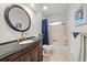 Bathroom with a black vanity, granite countertop, round mirror and a shower/tub combination with tile and blue accents at 5350 Barbarossa Ave, Sarasota, FL 34235