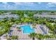 Aerial view of the community pool with surrounding lounge chairs, umbrellas, landscaping, and nearby buildings at 8827 Manor Loop # 208, Lakewood Ranch, FL 34202