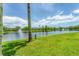 Scenic view of a serene pond surrounded by lush green grass, mature trees, and charming townhouses under a partly cloudy sky at 8827 Manor Loop # 208, Lakewood Ranch, FL 34202