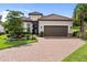 Charming single-story home with a red tile roof, brown garage door, brick driveway, and lush landscaping at 4735 Cassio Ct, Bradenton, FL 34211