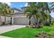 Two-story gray home featuring a gray garage door, tropical landscaping, and a green lawn at 16419 Paynes Mill Dr, Bradenton, FL 34211