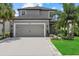 Two-story gray home featuring a gray garage door, tropical landscaping, and a lush lawn at 16419 Paynes Mill Dr, Bradenton, FL 34211