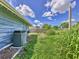 The overgrown backyard shows the side of the house and an air conditioning condenser at 2818 Olympic St, Sarasota, FL 34231