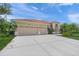 Beige single-story home featuring a three car garage, tile roof and beautiful landscaping with mature palm trees at 2937 Seasons Blvd, Sarasota, FL 34240