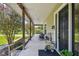 Spacious covered front porch with seating, wooden railings, and views of the surrounding greenery and blooming trees at 7264 Spencer Parrish Rd, Parrish, FL 34219