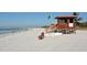 Lifeguard stand on a white sand beach with a green flag, bench, and rescue surfboard at 1 Benjamin Franklin Dr # 93, Sarasota, FL 34236