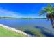 Scenic lake view with lush green lawn, a rocky shoreline, and palm trees under a clear sky at 10571 Old Grove Cir, Bradenton, FL 34212