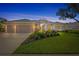 Charming home exterior at dusk, showcasing a well-lit facade, three-car garage, and lush landscaping at 11250 Rivers Bluff Cir, Lakewood Ranch, FL 34202
