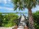 A wooden dock leads to tranquil waters, offering scenic views framed by verdant foliage and a swaying palm tree at 4907 Topsail Dr, Nokomis, FL 34275