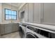 Bright laundry room with modern washer and dryer, grey cabinetry, and a window over the sink at 670 Old Compass Rd, Longboat Key, FL 34228