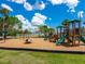A vibrant community playground featuring slides, swings, and climbing structures, set against a backdrop of blue skies and scattered clouds at 2416 Emory Ave, Bradenton, FL 34207