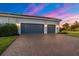 Three-car garage with brick paver driveway, exterior lighting, and manicured landscaping at 408 166Th E St, Bradenton, FL 34212