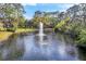 Scenic view of a pond featuring a fountain, surrounded by mature trees and greenery at 7674 Fairway Woods Dr # 1605, Sarasota, FL 34238