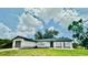Well-manicured lawn and a charming one-story house featuring an attached garage and a dark roof against a cloudy blue sky at 5009 Jody Ave, North Port, FL 34288