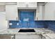Close-up of a modern kitchen showcasing granite countertops, a deep sink, and a stylish blue tiled backsplash at 528 Manor Dr, Dunedin, FL 34698