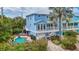 A bright blue home featuring a pool, outdoor spiral staircase, lush greenery, and brick-paved driveway at 202 75Th St, Holmes Beach, FL 34217