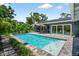 Backyard pool featuring a sun shelf, lush landscaping, a lounge area, and solar panels on the roof at 2460 Hillview St, Sarasota, FL 34239