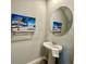 A half bathroom with a pedestal sink, oval mirror and beach themed art at 5812 Ocean Isle Dr, Nokomis, FL 34275