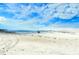 Expansive beach scene with clear blue sky, calm ocean waves, and a person walking with a surfboard at 701 Marbury Lane, Longboat Key, FL 34228