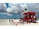 Red lifeguard stand on the beach with American and green flag displayed on a partly cloudy day at 915 Beach Rd # 321, Sarasota, FL 34242