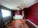Cozy bedroom with dark red accent walls, ceiling fan, an area rug with botanical accents and window at 1405 Dorchester St, Port Charlotte, FL 33952