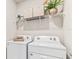 Functional laundry room equipped with a white washer and dryer, and upper shelving with decorative items at 16390 Bridle Ridge St, Port Charlotte, FL 33953