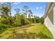 Image of the backyard featuring a white house, green trees, grass, and blue water tanks at 2643 Rushmore St, North Port, FL 34288