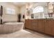 Bright bathroom featuring a soaking tub, natural wood cabinets and double sinks, and a large mirror at 15600 Aldama Cir, Port Charlotte, FL 33981