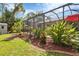 A view of the home's screened-in pool with beautiful tropical landscaping and a well-kept lawn at 1205 Bartlett Ave, North Port, FL 34288