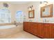 Bright main bathroom featuring dual sinks, soaking tub under arched window, and tiled floors at 3663 Whippoorwill Blvd, Punta Gorda, FL 33950