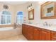 Bright main bathroom featuring dual sinks, soaking tub under arched window, and tiled floors at 3663 Whippoorwill Blvd, Punta Gorda, FL 33950