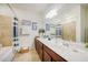 A bathroom with a dark wood vanity, large mirror, tub shower with blue accents, and tiled floor at 20272 Lagente, Venice, FL 34293