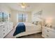 A cozy bedroom features a white bed dressed in blue, complemented by white furniture and plenty of natural light at 20272 Lagente, Venice, FL 34293