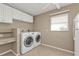 Functional laundry room features a modern washer and dryer, built-in desk and storage cabinets, and neutral tile flooring at 9428 Bandera Ln, Port Charlotte, FL 33981