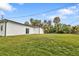 Exterior view of the backyard featuring a large grassy area, a white stucco house, and tall palm trees at 1117 Vernon Ave, Port Charlotte, FL 33948