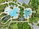 Aerial view shows a community pool with a lazy river, a slide, lounge chairs, palm trees, and lush landscaping at 12492 Shimmering Oak Cir, Venice, FL 34293