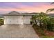 Exterior view of home highlighting three-car garage, and tropical landscaping against a sunset at 17917 Wayside Bnd, Punta Gorda, FL 33982