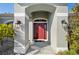 Close-up of a covered front entry with a striking red door, sconce lighting, and decorative stone landscaping at 17 White Marsh Ln, Rotonda West, FL 33947