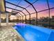 Backyard pool enclosed within a screened lanai, featuring cool blue water, brick pavers, and a scenic sunset view at 260 Long Meadow Ln, Rotonda West, FL 33947