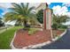 Community signage with landscaping and a palm tree add curb appeal to the entrance of the building at 3006 Caring Way # 329, Port Charlotte, FL 33952