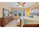 Bright bedroom with a wooden bed frame, ceiling fan, and three windows, complemented by a dresser with a mirror at 10357 Crooked Creek Dr, Venice, FL 34293
