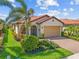 Charming single-story home featuring a tile roof, two-car garage, and lush tropical landscaping in the front yard at 10357 Crooked Creek Dr, Venice, FL 34293