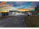 Single-story home featuring stucco walls, curved window accents, and a concrete driveway under a colorful sky at 3243 Elkcam Blvd, Port Charlotte, FL 33952