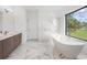 Bright bathroom features a soaking tub next to a large window with a view and marble tile floor and walls at 24259 Peppercorn Rd, Punta Gorda, FL 33955