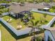 Aerial view of a fenced backyard with a screened-in lanai, mature palm trees, and green lawn at 15288 Mille Fiore Blvd, Port Charlotte, FL 33953