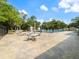 The community pool features ample seating with tables and chairs, shaded by umbrellas and surrounded by lush trees at 478 Winwood Ct, Port Charlotte, FL 33954