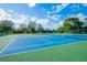A view of newly painted blue and green tennis courts surrounded by a green fence and lush trees at 1065 Harbour Glen Pl, Punta Gorda, FL 33983