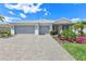 Single-story home featuring a spacious three-car garage and beautiful landscaping with colorful flower beds and a brick driveway at 16064 Shoreline Dr, Punta Gorda, FL 33982